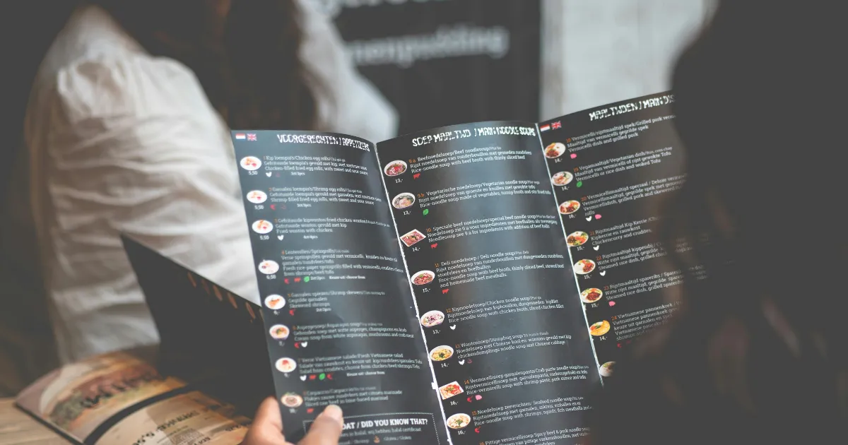 Cliente segurando o cardápio aberto de um restaurante, com vários pratos e preços listados