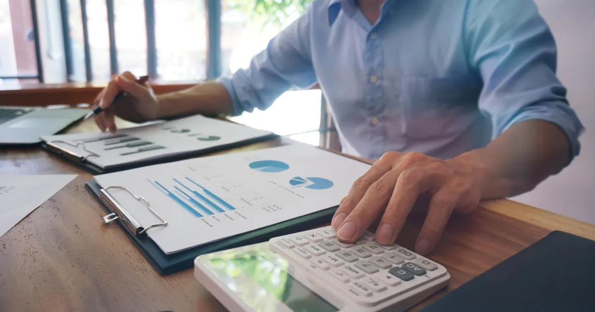 Dono de restaurante analisando gráficos e planilhas com uma calculadora, tentando entender para onde vai o dinheiro do faturamento